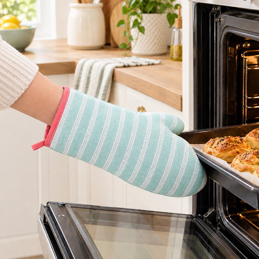 Green striped single oven glove worn while removing a baking dish from the oven