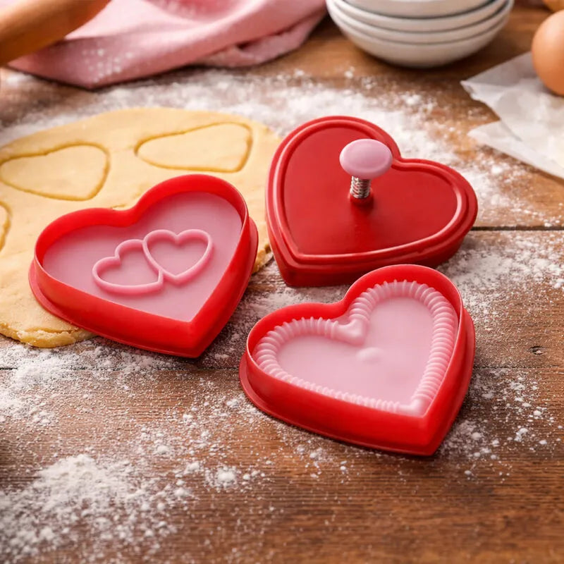 Red heart cookie cutter set with plunger stamps on rolled dough next to cut heart cookies