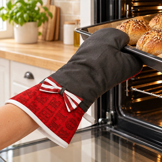 Red heat-resistant single oven mitt with bow detail being used to pull a hot tray from the oven
