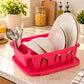 Pink dish drainer with white plates and cutlery on a marble kitchen counter