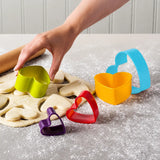 Set of 5 colorful heart shape cookie cutters in different sizes being pressed into rolled cookie dough