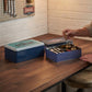 Set of 2 navy blue metal kitchen storage tins with handles sitting on a wooden kitchen table