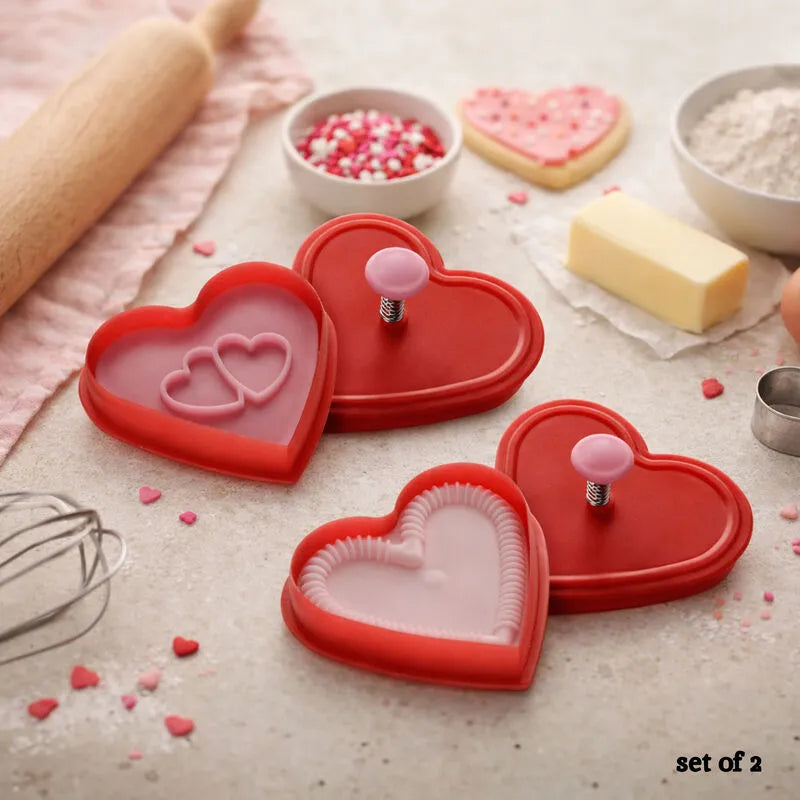 Red heart shaped plunger cookie cutter set with stamped heart cookies and sprinkles on a baking table