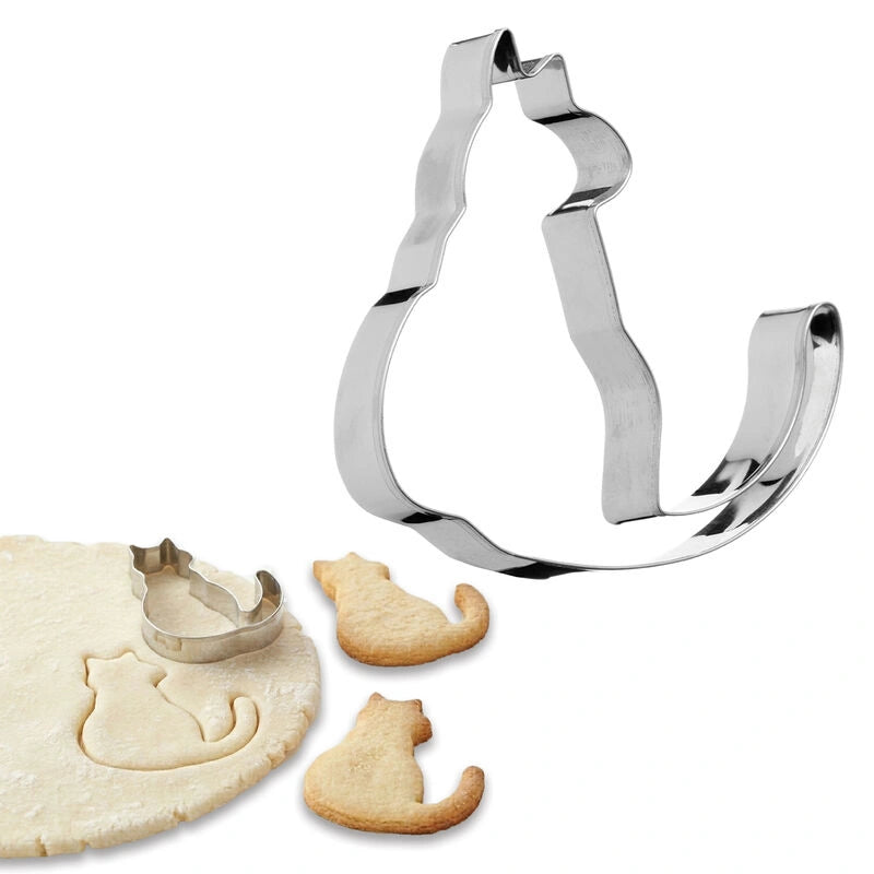 Silver cat cookie cutter beside baked cat shaped sugar cookies on rolled dough