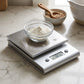Silver digital kitchen scale weighing a bowl of flour on marble countertop
