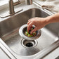 Stainless steel sink strainer catching vegetable scraps while rinsing in the sink.