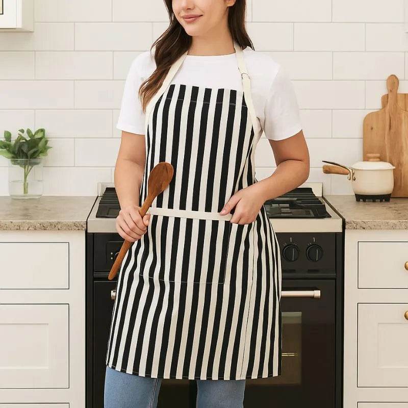 white and black apron with front pocket worn by woman holding wooden spoon, striped cotton kitchen apron for women
