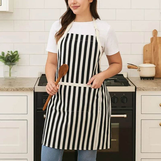 white and black apron with front pocket worn by woman holding wooden spoon, striped cotton kitchen apron for women