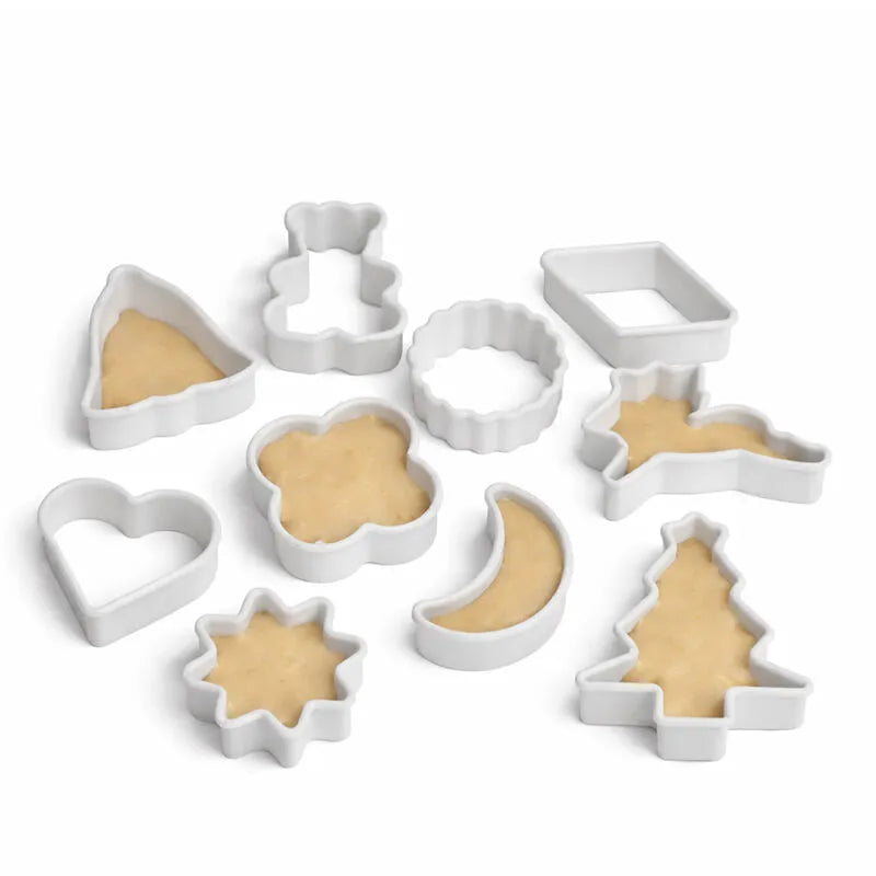 White cookie cutter set with heart, star, moon and tree shapes beside matching baked cookies on a white background
